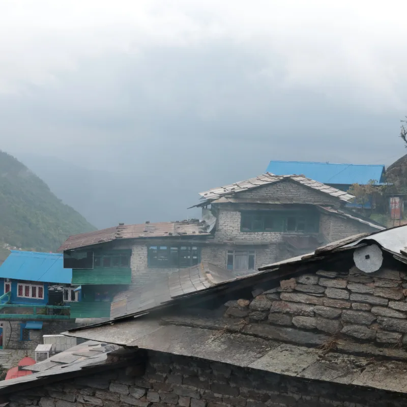 Traditional stone teahouses with slate and blue roofs nestled on a steep, misty mountain hillside in Ulleri village.