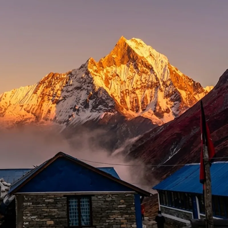 Traditional stone trekking lodge in a valley beneath the golden sunlit summit of Fishtail Mountain Machapuchare.