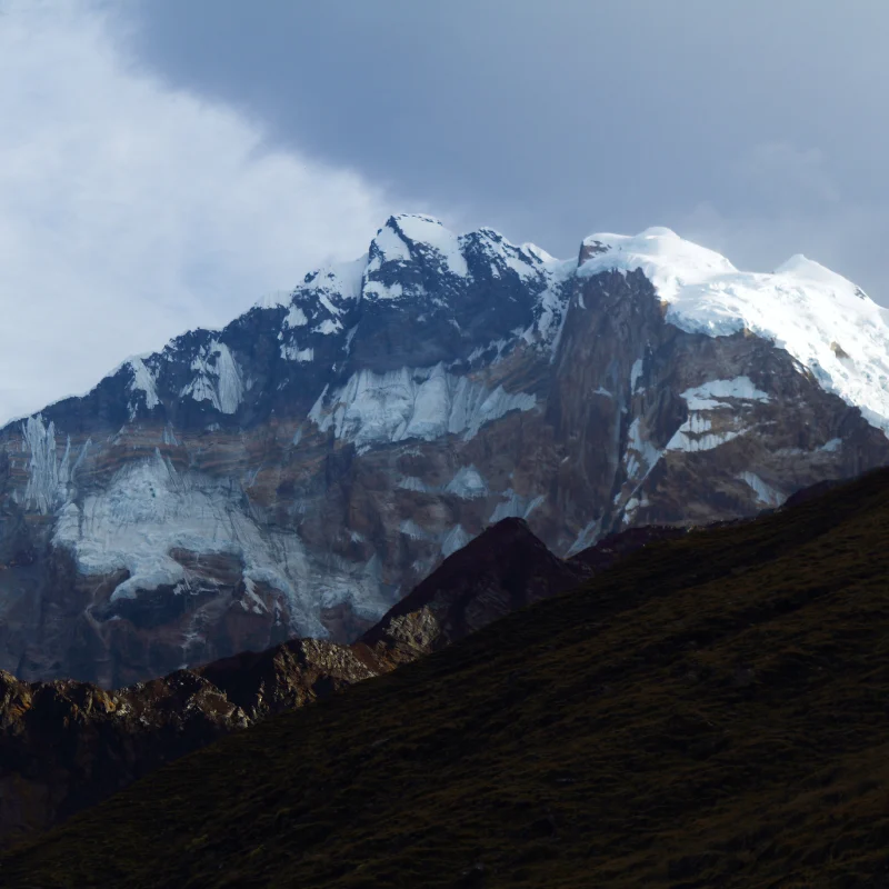 Massive snow-covered Himalayan mountain peak rising above dark alpine slopes seen from Khopra Danda viewpoint Nepal.