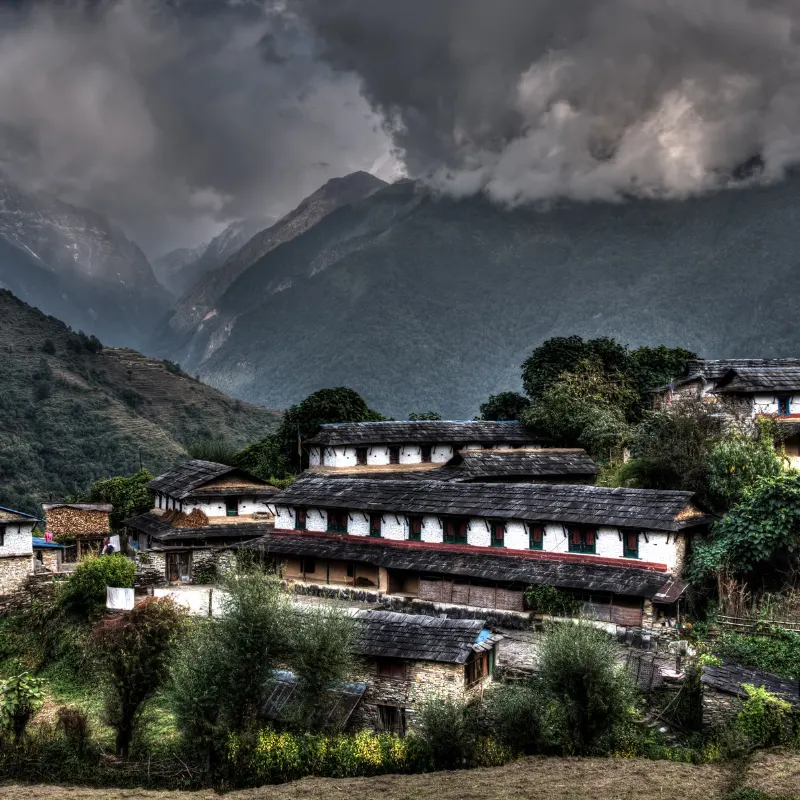 Traditional slate-roofed Gurung houses of Ghandruk village under dark dramatic clouds with Himalayan foothills in the background Nepal.