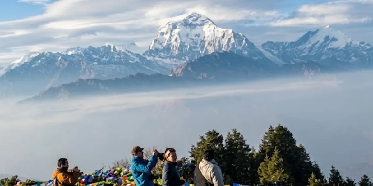 Hikers taking photos from a high viewpoint overlooking a sea of low clouds and the massive snow-capped Dhaulagiri peak.