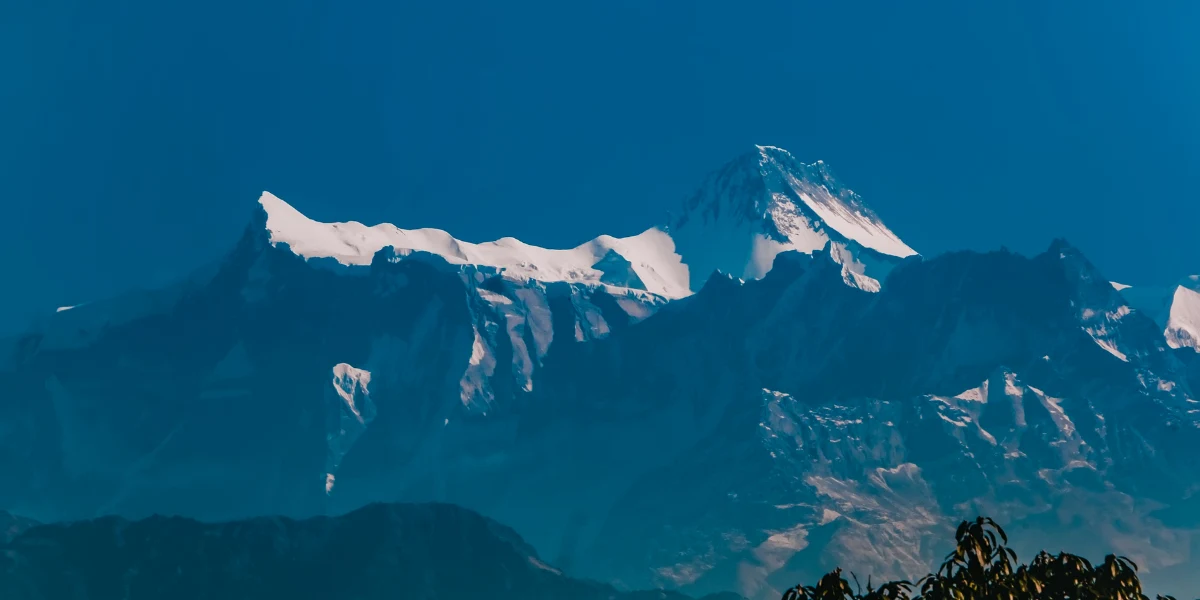 Sharp, snow-covered summits of Lamjung Himal against a clear, deep blue sky in central Nepal.