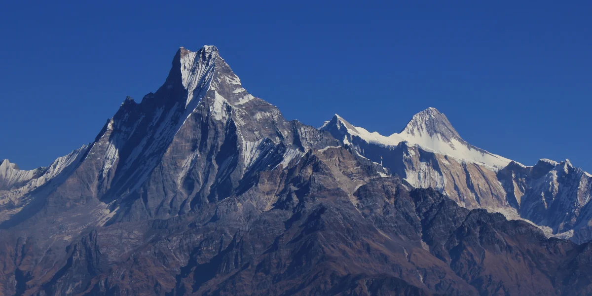 Majestic view of Machapuchare Fishtail peak with steep snow-dusted ridgelines set against a clear blue sky.